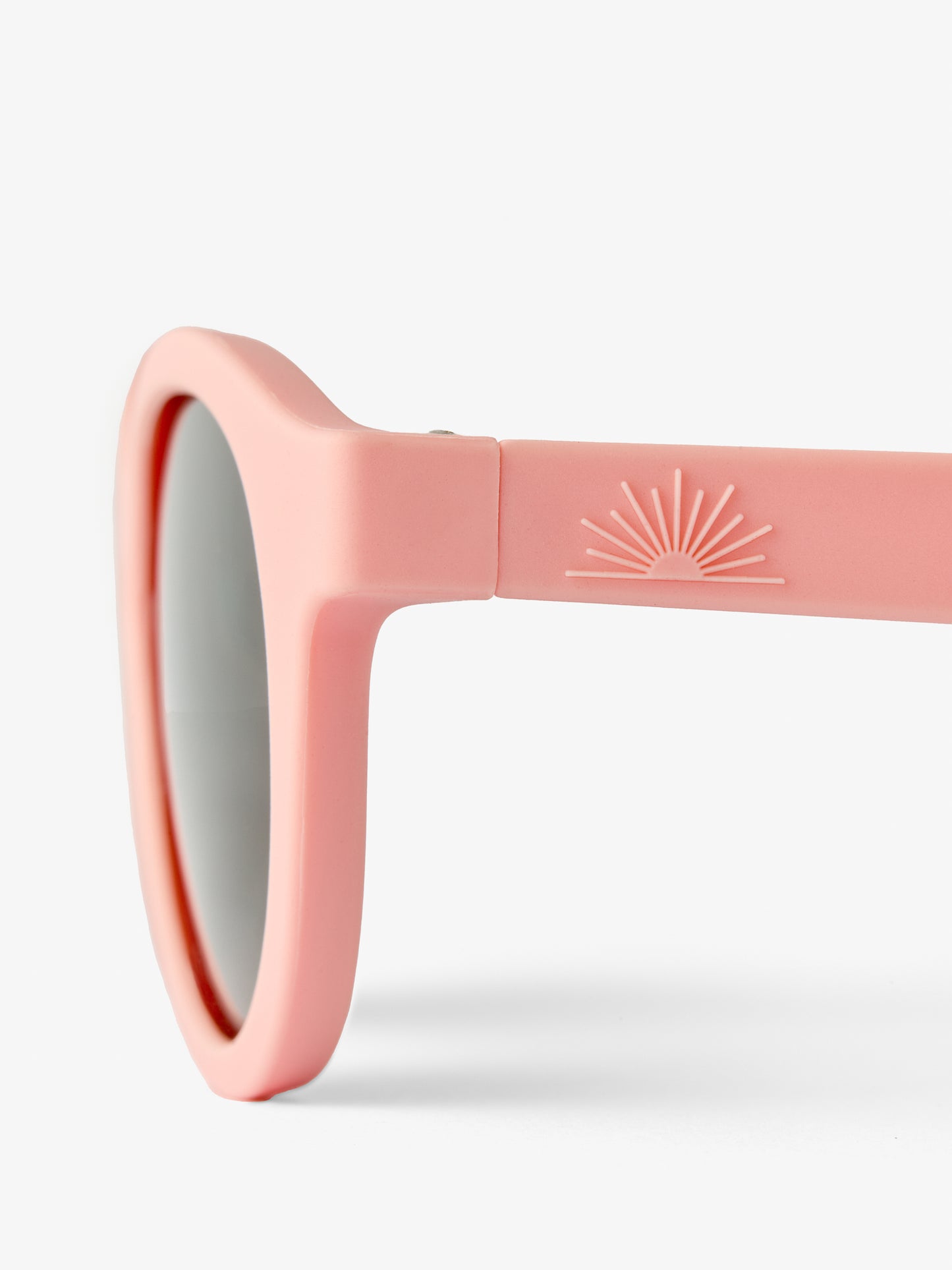 Close up of side of round pink baby sunglasses by Petit Peepers showing half sun logo